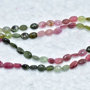 May include: A strand of oval-shaped gemstone beads in shades of pink, green, and black. The beads are strung on a clear thread and are arranged in a graduated pattern.