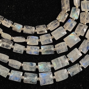 Puede incluir: Una hebra de cuentas de piedra lunar blanca con forma rectangular. Las cuentas están enhebradas en alambre plateado.