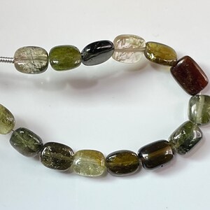 Può includere: Una collana di perline di pietre preziose sfaccettate di colore verde, marrone e trasparente. Le perline sono rettangolari e hanno una finitura liscia e lucida.