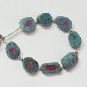 May include: A strand of blue and green gemstone beads with pink accents. The beads are oval shaped and strung on a silver chain. The chain has two tassels on one end.