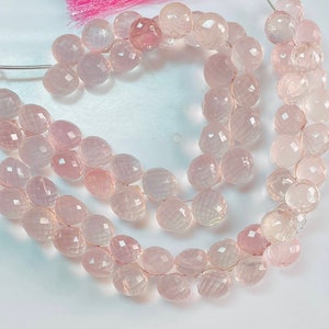 May include: A strand of pale pink faceted gemstone beads. The beads are round and have a slightly translucent appearance.