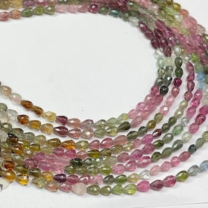 Può includere: Un filo di perline di pietre preziose multicolori, con un mix di perline a forma di goccia rosa, verde e marrone. Le perline sono infilate su un filo trasparente e sono disposte in un motivo sciolto e fluido.