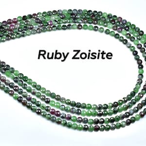 May include: A strand of green and pink Ruby Zoisite beads. The beads are faceted and have a round shape.