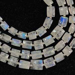 Puede incluir: Una hebra de cuentas de piedra lunar blanca con un brillo iridiscente arcoíris. Las cuentas son rectangulares y facetadas, y están enhebradas en alambre plateado.