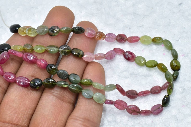 May include: A strand of oval-shaped, multi-colored gemstone beads. The beads are shades of green, pink, and black.