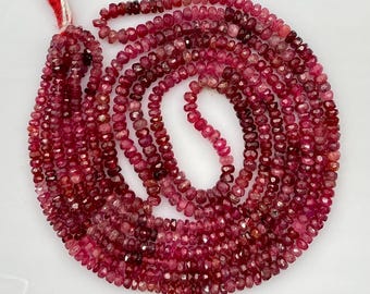 May include: A strand of small, faceted, round beads in varying shades of deep pink and dark red. The beads are strung together on a thin cord, creating a circular arrangement with a red thread tail extending from the top left corner.