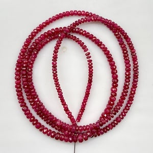 Peut inclure: Un long collier composé de petites perles de pierres précieuses facettées d'un rouge rosé profond, disposées en boucle circulaire avec une section centrale tombante. Les perles sont uniformes, avec une surface facettée qui reflète la lumière.