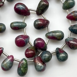 May include: Close-up of gemstone beads in shades of red, teal, and green. The teardrop-shaped beads are strung together with silver-coloured wire. The beads are approximately 1-2 cm in length, creating a natural aesthetic.