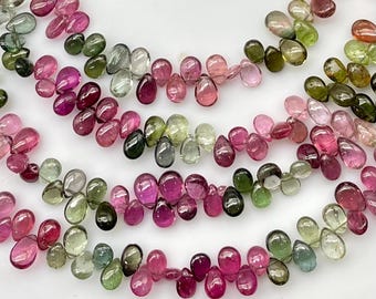 May include: A collection of loose, teardrop-shaped tourmaline gemstones in various shades of pink, magenta, and green. The stones are polished and translucent, displaying natural color variations and internal inclusions across the assortment.