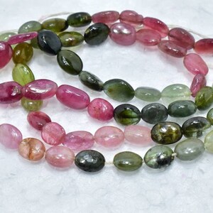 May include: A strand of oval-shaped, multi-colored tourmaline beads. The beads are a mix of pink, green, and yellow.