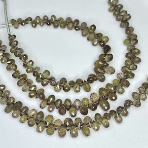 May include: Three strands of faceted green gemstone beads, each strand is composed of small, teardrop-shaped beads. The beads are strung on a silver wire.