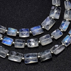 Puede incluir: Una hebra de cuentas de piedra lunar iridiscente, cada cuenta tiene una forma rectangular con un acabado liso y pulido. Las cuentas están enhebradas en alambre de plata.