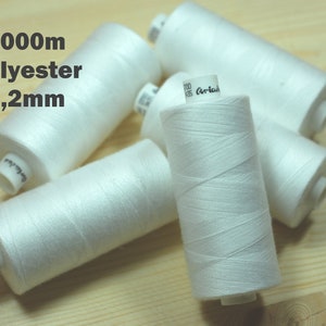 Könnte beinhalten: Fünf Spulen weißen 1000 m Polyestergarns, jede 0,2 mm dick. Die Spulen liegen auf einer Holzoberfläche.