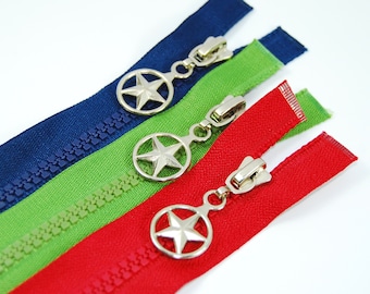 May include: Close-up of three zippers in red, green, and blue. Each zipper has a silver pull with a star design. The zippers are angled, showcasing their color and detail against a white background. These are likely for sewing or craft projects.