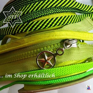 May include: A coiled lime green zipper featuring a metallic silver star-shaped pull tab. The zipper is layered with a black and lime green striped fabric trim. The text SET is visible in a white star outline, and the text im Shop erh&auml;ltlich is present.