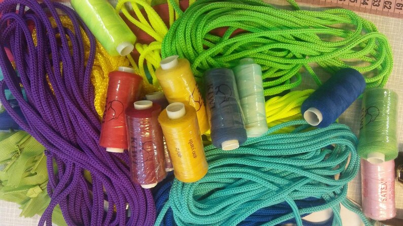 May include: A collection of vibrant craft supplies including coiled lengths of purple, lime green, yellow, and turquoise cord alongside various spools of sewing thread in red, yellow, dark blue, light blue, green, and pink colors.