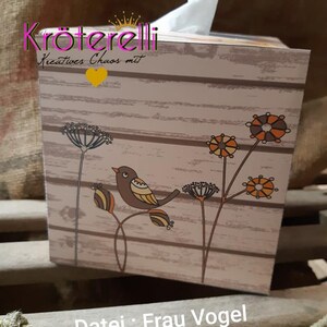 May include: A decorative tissue box with a wooden plank design. The box features a brown bird perched on a branch with orange and brown accents. The text "Datei: Frau Vogel" is visible on the box.