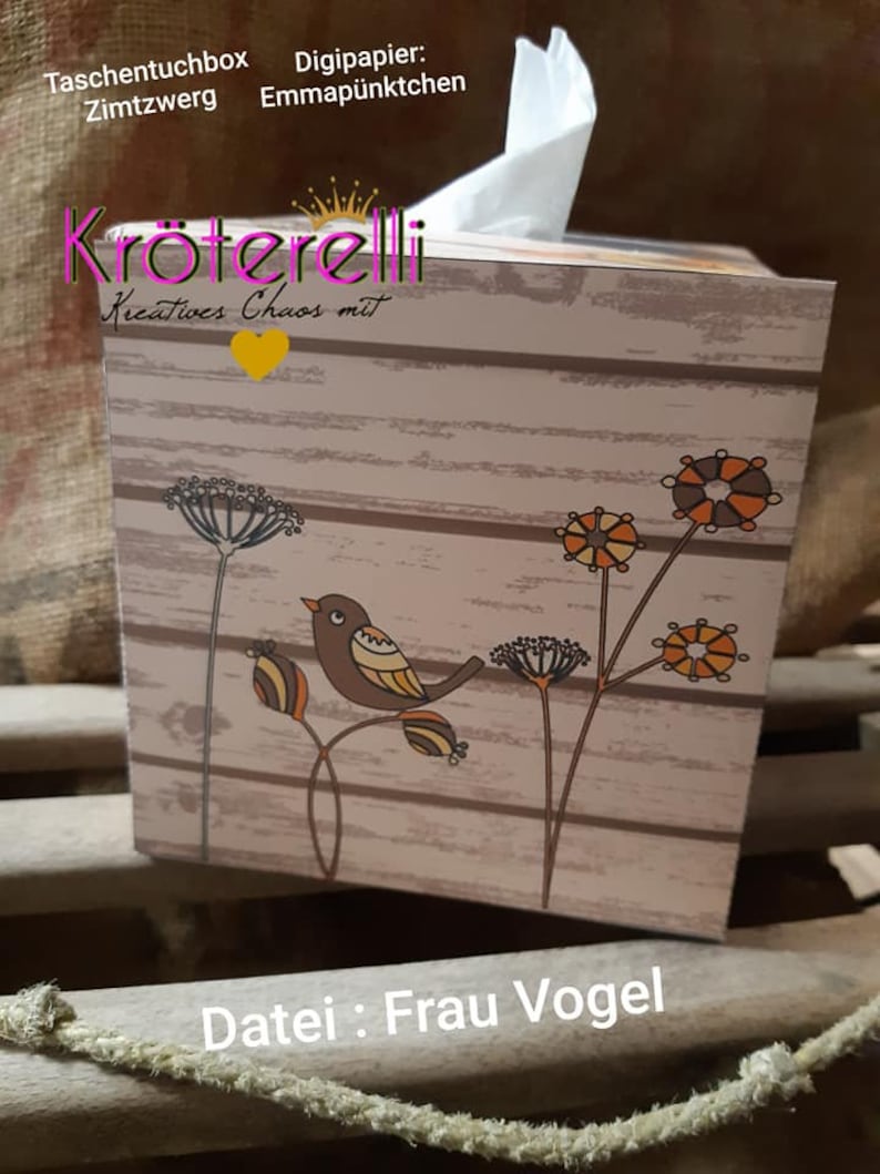 May include: A decorative tissue box with a wooden plank design. The box features a brown bird perched on a branch with orange and brown accents. The text "Datei: Frau Vogel" is visible on the box.