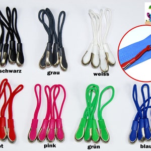 Könnte beinhalten: Sortiment an Reißverschluss-Zierbändern in verschiedenen Farben, darunter Schwarz, Grau, Weiß, Rot, Pink, Grün und Blau. Jeder Zipper hat eine silberne Metallschlaufe und eine Kordel.