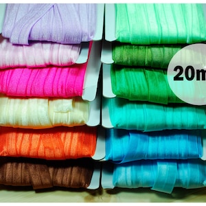 Könnte beinhalten: Ein Stapel 20 mm breiter, bunter Satinband in verschiedenen Farben, darunter Lila, Pink, Weiß, Orange, Braun, Türkis und Grün. Das Band wird auf weißem Karton präsentiert.