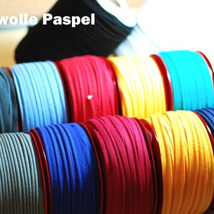 Könnte beinhalten: Eine Sammlung von 10 mm Baumwollpaspel in verschiedenen Farben, darunter Grau, Blau, Rot, Gelb und Türkis, auf Spulen gewickelt.