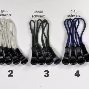 Könnte beinhalten: Fünf Sätze Reißverschluss-Zipper, jeder Satz enthält drei Zipper. Die Zipper sind schwarz mit einem weißen, grauen, khaki, blauen und schwarzen Band. Die Bänder sind oben in einer Schlaufe gebunden. Die Sätze sind von 1 bis 5 nummeriert.