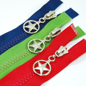 Könnte beinhalten: Drei Reißverschlüsse mit sternförmigen Metall-Anhängern. Die Reißverschlüsse sind in Blau, Grün und Rot.