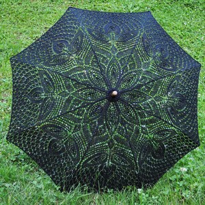 Könnte beinhalten: Ein schwarzer Spitzenschirm mit einem Holzgriff. Die Spitze hat ein zartes Blumenmuster.