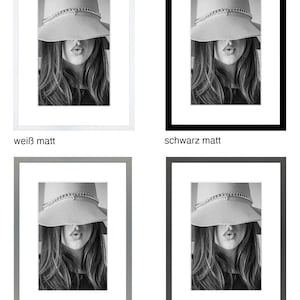 May include: A black and white photo of a woman wearing a hat. The hat is covering her eyes and she is looking at the camera. The photo is framed in a white, black, light gray, or dark gray frame.