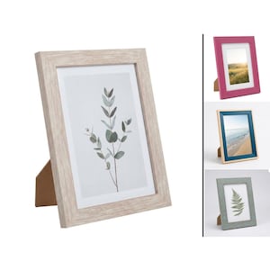 Könnte beinhalten: Eine Sammlung von gerahmten Kunstdrucken. Der Hauptrahmen ist hell holzfarben und zeigt einen botanischen Druck. Zusätzliche Rahmen in Pink, Blau und Grün sind ebenfalls abgebildet, jeder mit einem anderen Bild. Alle Rahmen haben einen Ständer für die Tischpräsentation.