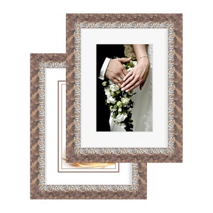 Puede incluir: Dos marcos de fotos ornamentados con un patrón de espiral decorativo. Los marcos son de madera y tienen un acabado marrón. El marco más grande está encima del marco más pequeño. El marco más pequeño tiene un paspartú blanco y una foto de una novia y un novio sosteniendo un ramo de flores blancas.