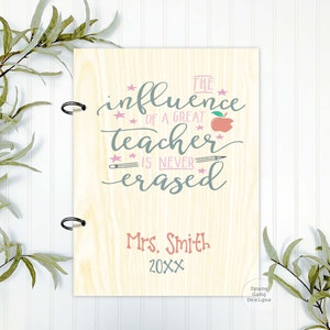 May include: A wooden sign with a light brown background and a white inscription that reads "The influence of a great teacher is never erased." The sign also includes a red apple, a pencil, and stars. The text "Mrs. Smith 20XX" is written in pink at the bottom of the sign.