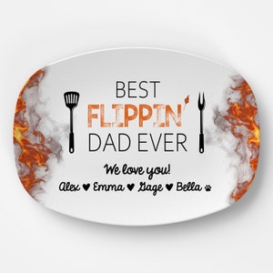 May include: White oval serving platter with a black and orange design of flames and smoke. The text "BEST FLIPPIN' DAD EVER" is printed in black with a red outline. Below the text is "We love you!" and the names "Alex, Emma, Sage, Bella" with hearts and a paw print.