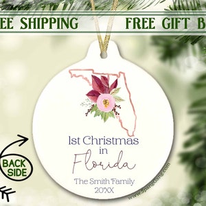 May include: White ceramic ornament with a pink and burgundy floral design and an outline of the state of Florida. The text "1st Christmas in Florida" is written below the floral design, followed by "The Smith Family 20XX".