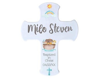 May include: A light blue wooden cross with a rainbow, sun, and clouds at the top. The cross has the name "Milo Steven" written in gray text and the words "Baptized in Christ 04/23/XXX" written in black text. The cross also features a watercolor illustration of Noah's Ark with animals.