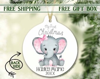 May include: A white round Christmas ornament with a pink and gray elephant illustration. The ornament says "My First Christmas" and is personalized with the name "Hayley Marie" and the year "20XX".