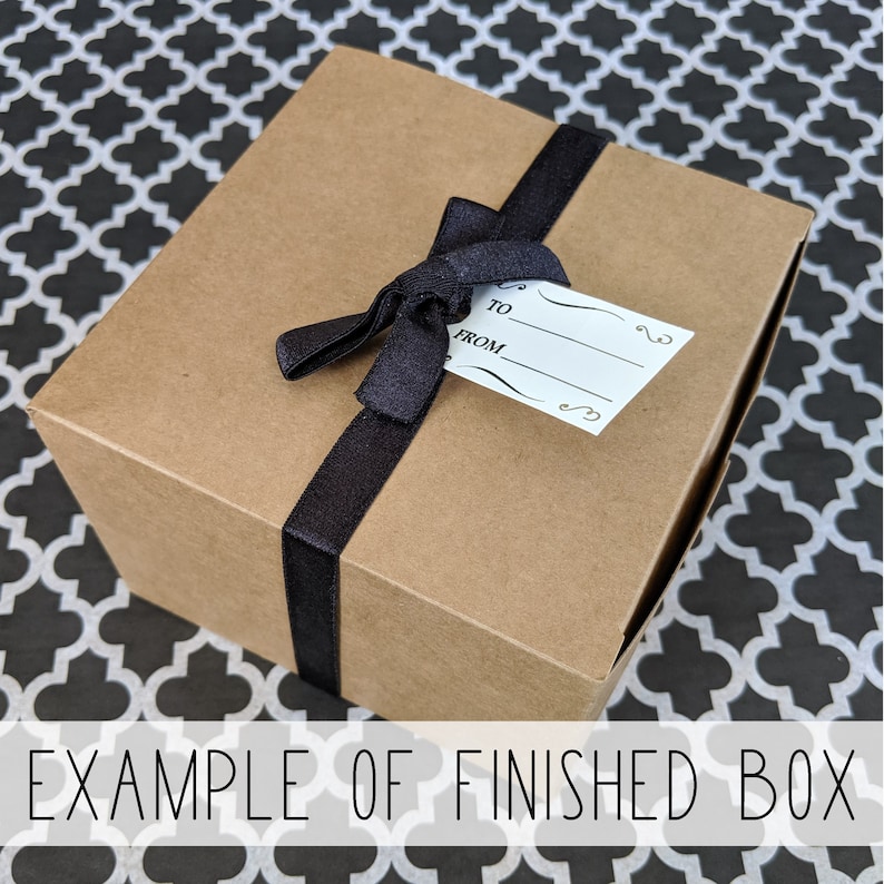 May include: A brown cardboard gift box with a black ribbon and bow. The box has a white gift tag with the words "To" and "From" printed on it.