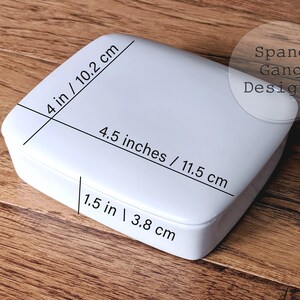 May include: White square box with measurements in inches and centimeters. The box is 4 inches by 4.5 inches by 1.5 inches. The text "Spang Gang Designs" is printed on the box.