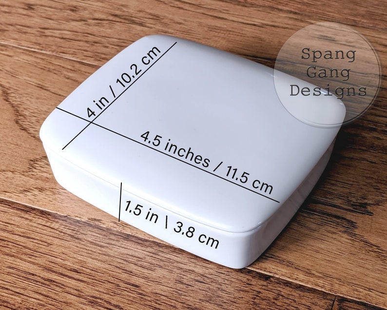 May include: White square box with measurements in inches and centimeters. The box is 4 inches by 4.5 inches by 1.5 inches. The text "Spang Gang Designs" is printed on the box.