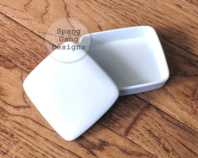 May include: White ceramic square box with a lid. The box is open and the lid is sitting next to it.