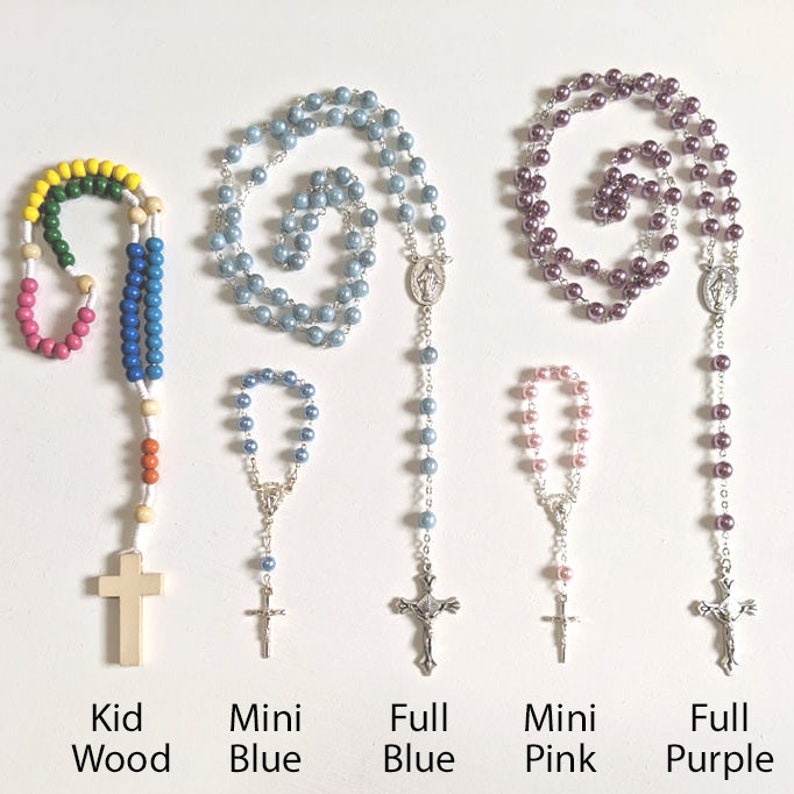 May include: Five different rosaries, including a wooden kid's rosary, a mini blue rosary, a full-size blue rosary, a mini pink rosary, and a full-size purple rosary.