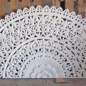 Op de afbeelding: Wit houten hoofdbord met ingewikkelde gesneden bloemmotieven. Het hoofdbord is halfrond en heeft een grote bloem in het midden.
