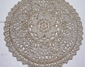 May include: A round, white wooden wall decor with intricate floral carvings. The design features a large central flower surrounded by smaller floral motifs.