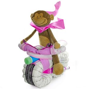 Puede incluir: Un mono de peluche con una bufanda rosa monta una motocicleta de pastel de pañales. La motocicleta está decorada con cintas rosas y blancas y tiene una botella azul y verde unida al frente.