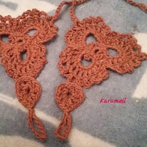May include: A pair of crocheted foot jewelry in a brown color. The jewelry is made of a delicate, lacy pattern and has a simple design. The jewelry is tied with a string at the ankle.