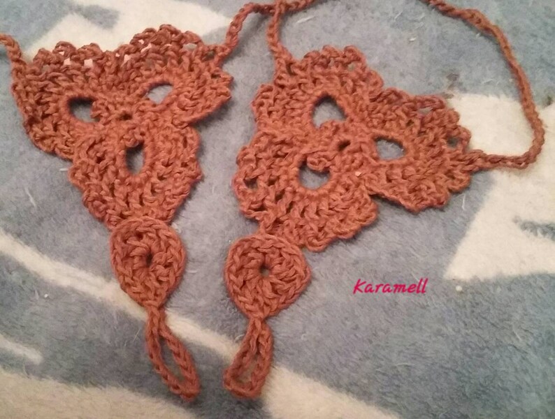 May include: A pair of crocheted foot jewelry in a brown color. The jewelry is made of a delicate, lacy pattern and has a simple design. The jewelry is tied with a string at the ankle.