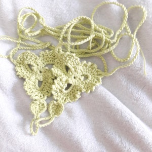 May include: A light green crocheted piece with a delicate pattern. The piece is made of yarn and has a loose, flowing texture.