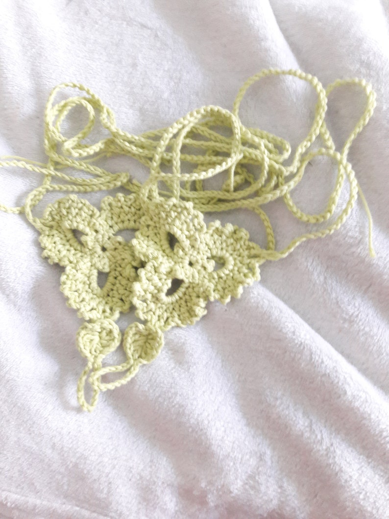 May include: A light green crocheted piece with a delicate pattern. The piece is made of yarn and has a loose, flowing texture.