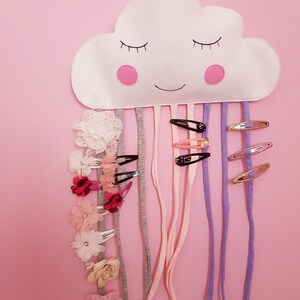 May include: A white felt cloud with a smiling face and pink cheeks, hanging from the ceiling.  It has multiple colorful ribbons and hair clips attached to it.