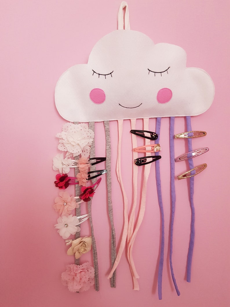 May include: A white felt cloud with a smiling face and pink cheeks, hanging from the ceiling.  It has multiple colorful ribbons and hair clips attached to it.